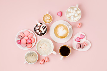 Various kinds of coffee in cups of different size with candys and macaroons on pale pink...