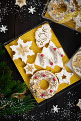 Gingerbread cookies gift set box with white icing, silver and golden sprinkles, snowflake, Christmas tree, stars and pig face on biscuits, dark wooden background, homemade sweets present, copy space 