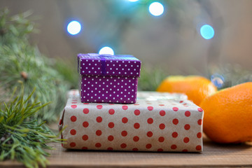 Two boxes with gifts, tangerines, a Christmas tree branch, lights on the background - a festive picture close-up. Festive winter mood.