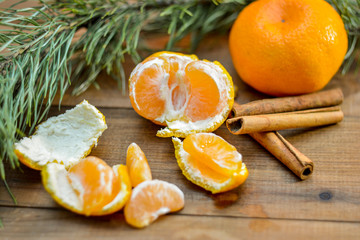 Tangerines, cinnamon sticks and a branch of spruce on a wooden background. Winter mood. In anticipation of Christmas and New Year.