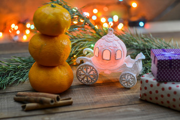 Fairy-tale story - a Cinderella carriage, a mandarin snowman, a spruce branch, a wooden background, boxes with Christmas presents.