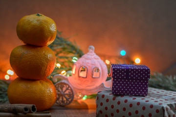 A snowman of three mandarins, a Cinderella carriage, a branch of spruce, christmas lights, boxes of gifts. Christmas fabulous picture. Good New Year spirit.