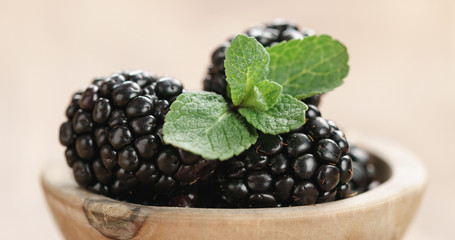 Closeup   of fresh blackberry with mint leaves in wooden bowl on table
