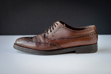 one brown shoes in profile on black background, illustration.