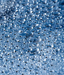 Closeup of water drops on a metal surface with holes in it.