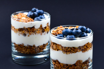 Homemade baked granola with yogurt and blueberries in a glass on a black background. Space for text or design.