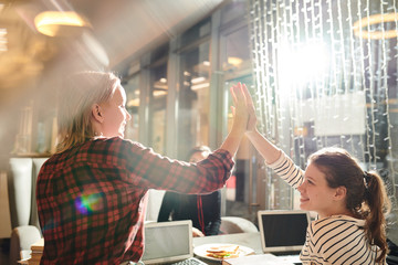 Happy teenagers giving five to each other during friendly collaboration on studying project