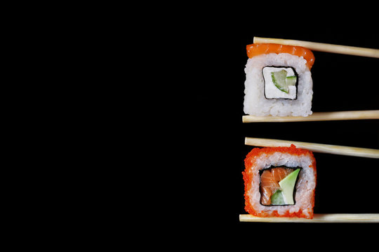 roll with salmon in chopsticks isolated on black