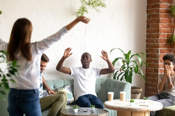 Happy smiling diverse good friends greeting woman in cafe, laughing excited African American man with raising hands saying hello to colleague, meeting in coffee house, sitting at table