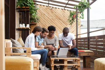 Diverse multiethnic smiling friends looking at laptop screen together on cafe terrace, multiracial...