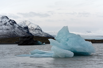 Glacier lagoon with a big blue iceberg in the foreground, in the background a dark iceberg and...