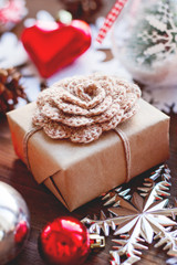 Christmas and New Year background with presents, ribbons, balls and different decorations on wooden background. Gift in Craft wrapping paper with hand made crocheted flower.