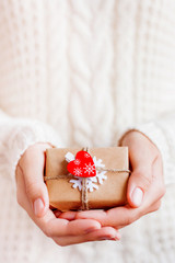 Woman in knitted sweater is holding Christmas present packed in craft paper with felt snowflake and red heart. New Year or St. Valentine Day DIY gift.