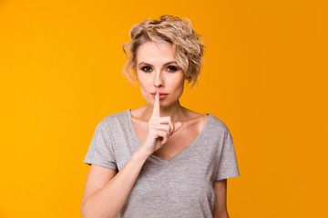 Silence. Woman asking for silence or secrecy with finger on lips hush hand gesture yellow background wall. Pretty girl placing fingers on lips, shhh sign symbol. Negative emotion facial expression