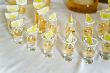 Good service of tequila in small glasses with lime on the white tablecloth. Glasses with vodka,...