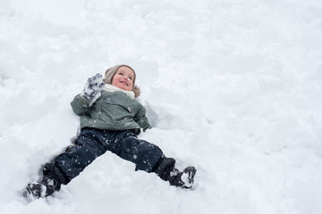 Fototapeta na wymiar Little boy in warm clothes enjoying first snow and having fun outdoor