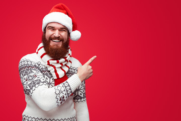 man in christmas clothes pointing away at copyspace isolated over red