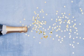 Champagne bottle with confetti stars on blue background. Holiday concept. Flat lay style. Copy space, top view. © Laima Gri