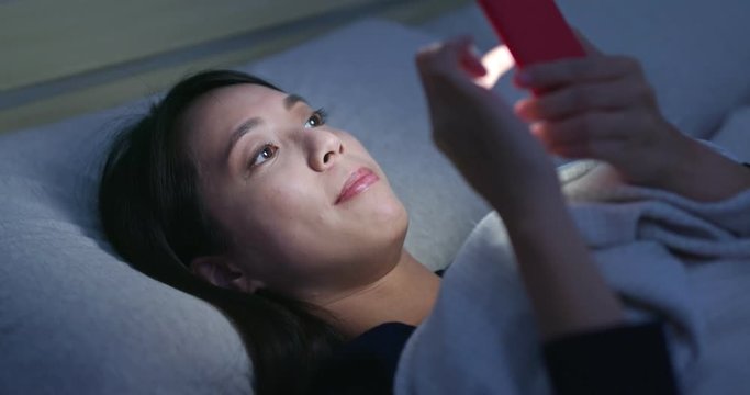 Woman watch on mobile phone and lying on bed at night