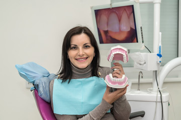 Woman in dentist chair holding jaw and smiling