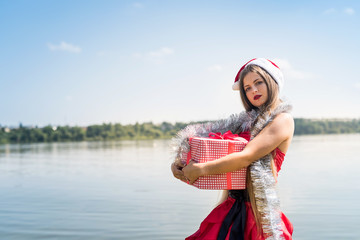 Beautiful girl santa holding gift box on seashore