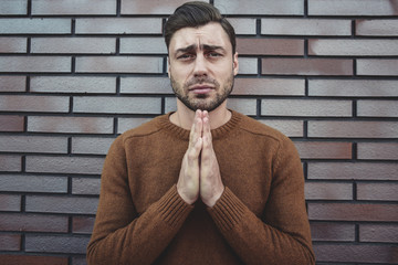 Asking for forgiveness .Religion concept. Caucasian young man praying against the gray brick wall.