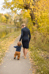 Fototapeta premium mom teaches son by the hand. mom holds the child's hand. autumn. autumn time. a mother and her child. little boy