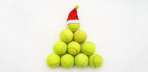 Santa hat on tennis ball on white snow background. Merry Christmas and New year concept with tennis balls. Yellow green color tennis balls in shape fir tree. Close up, sport lifestyle. Isolated,