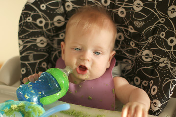 Small baby boy is tasting first food and learning how to eat with spoon in cute child feeding...
