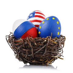 Obraz premium Three Easter eggs in a nest painted in colors of flags of Russia, America and the European Union, isolated on a white background. Friendship concept