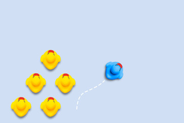 Group of yellow ducklings moves in one direction, but one blue duck swims in another direction. Blue background. The concept of innovative and creative business solutions. Flat lay, top view