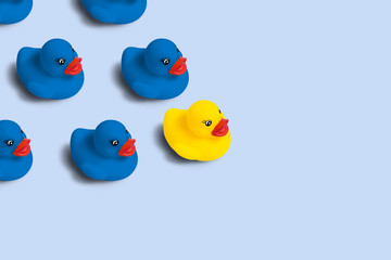 Group of blue toy ducks and one yellow duck in the head of the group on a blue background. Concept of creative business solutions, team leadership, stands out from the crowd, uniqueness