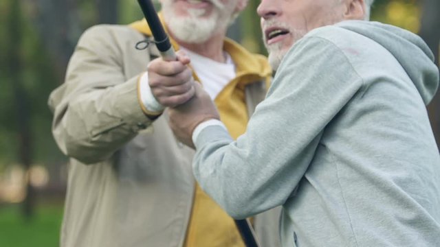 Bearded man helping his retired friend pulling fish out of water, male hobby