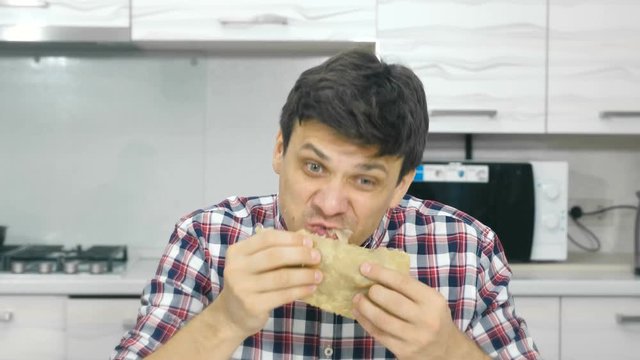 Young man in a plaid shirt quickly eats a big cheburek with an appetite, hurry.