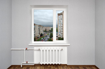 White window in empty room with heating and gray walls. Cityscape from the window of the home.
