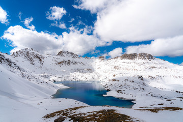 Fototapeta na wymiar A very deep blue lake sits in a valley between snow capped mountains on a partly cloudy day