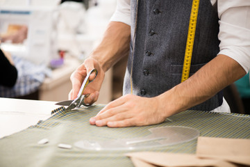 Close up portrait of unrecognizable male tailor cutting fabric and making patterns for clothes while working in traditional atelier workshop, copy space