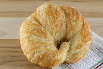 Single croissant roll on wooden cutting board with cloth.  Side view.  White background.