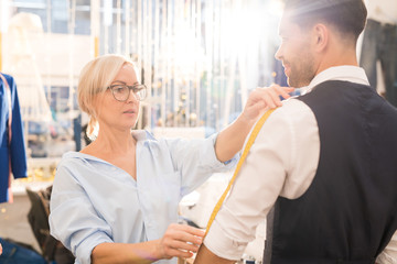 Waist up portrait of female tailor measuring client while fitting bespoke suit in traditional...
