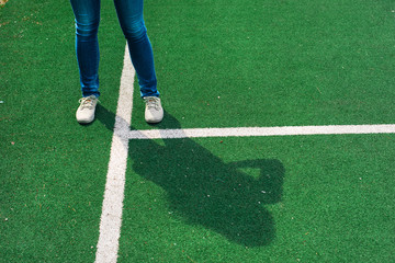 Obraz premium Young women in jeans and sports shoes staying on green footbal field next to white lines. Dropping shadow and showing signs. Concept. Copy space.