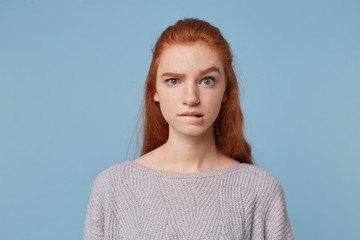 Young beautiful red-haired teen girl looks concerned puzzled in a panic, one eyebrow raised bit her...