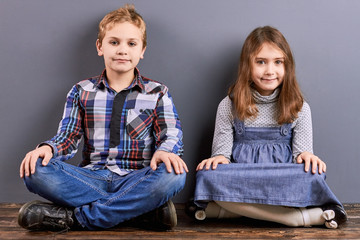 Two kids sitting with crossed legs. Studio portrait of little sister and brother sitting on floor...