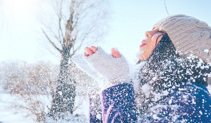 Winter girl portrait. Beauty joyful model girl blowing snow, having fun in winter park. Beautiful...