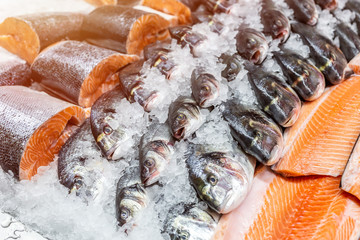 Fresh seafood on crushed ice at fish market. Raw dorado, seabass and salmon fillet on display...