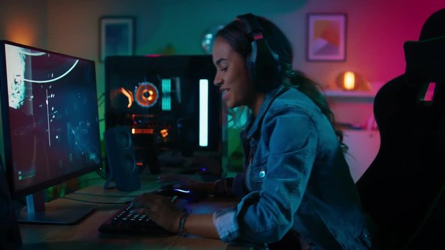 Pretty and Excited Black Gamer Girl in Headphones is Playing and Winning in First-Person Shooter Online Video Game on Her Computer