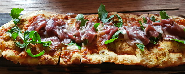  Flatbread with prosciutto cheese and arugula on wooden table.