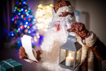 Santa Claus in a red suit reads the list of those who are waiting for gifts from him. Many gifts and a Christmas tree.