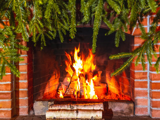 Burning firewood in a fireplace decorated for Christmas with branches of spruce