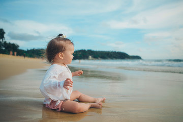 little girl in white clothes playing with sand on the beach among the waves