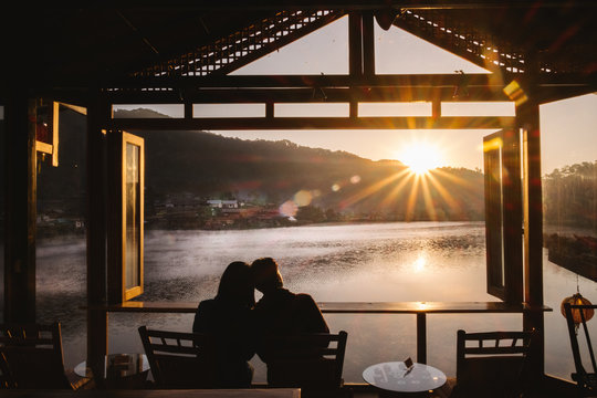 Asian couple look at Mountain Mist and riverside view from the wooden window and chair of Little Home at Ruk Thai in Mae Hong Sorn Province, Thailand